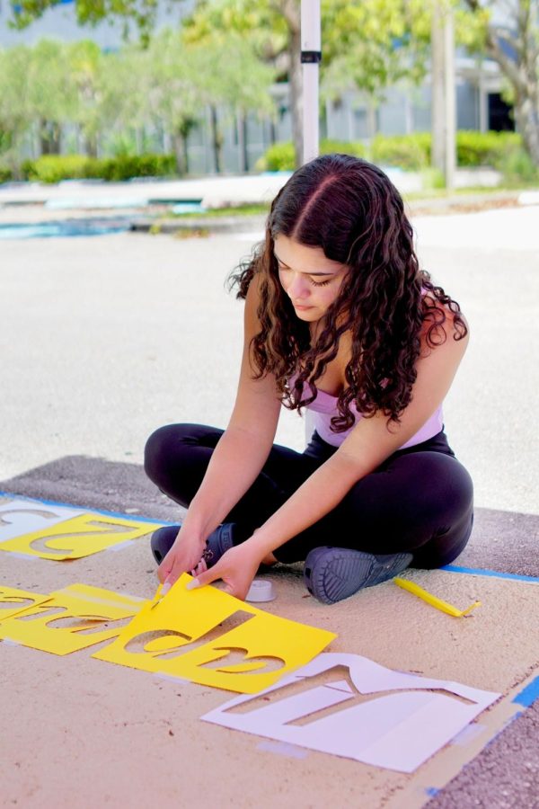 Making sure her stencils are placed perfectly, Maylene Aponte trims down the side of her Billie Eilish, Happier Than Ever inspired stencil. 