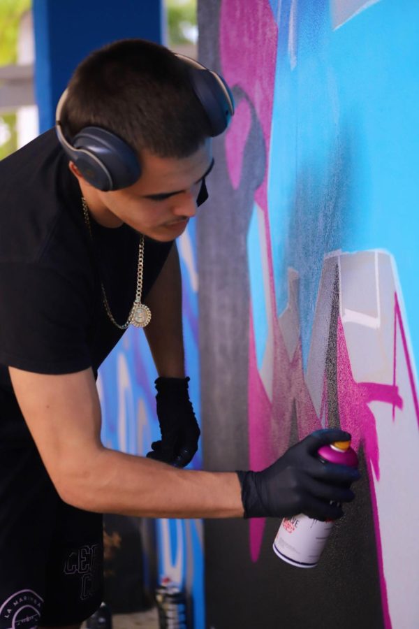 Senior Luis Arboleda applies magenta to the outline of the word BUCS on the mural. 