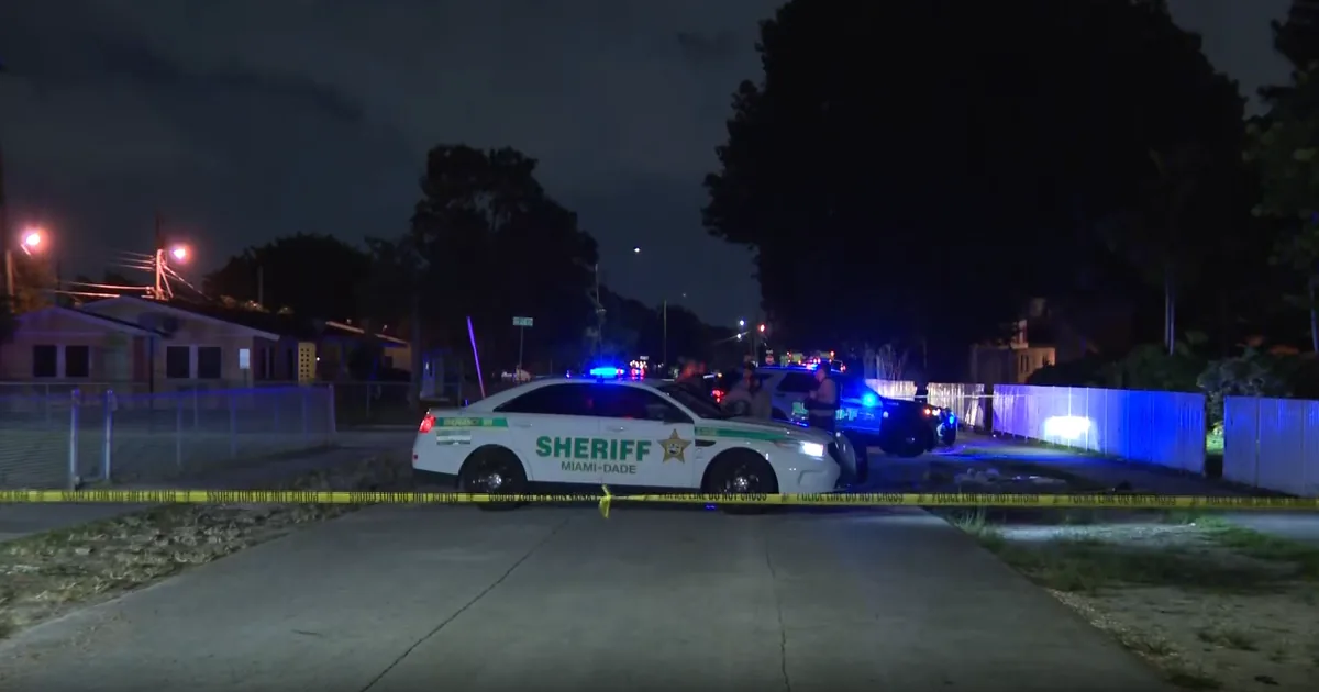 Police tape and emergency vehicles at a nighttime crime scene in Miami-Dade County